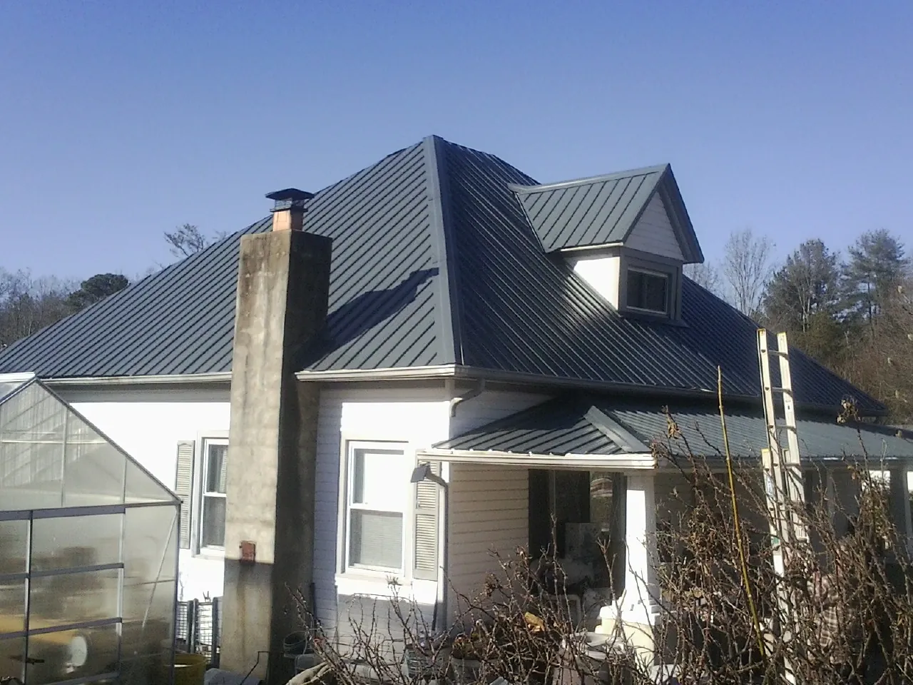 Dark blue standing seam metal roof on a white farmhouse with dormer — Slate & Tile Roof Repair by Roofing Brothers in Lake George