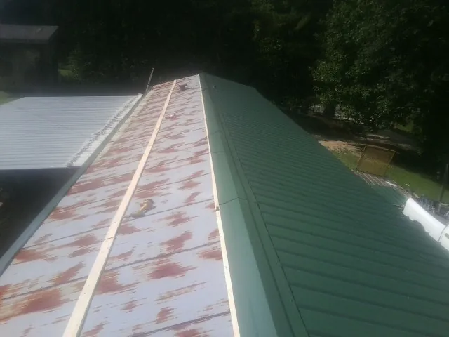 Old rusted panels beside newly installed green metal roofing — Wind Damage Roof Repair by Roofing Brothers in Lake George