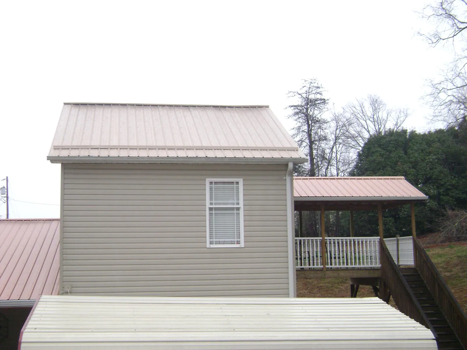 Tan metal roofs on a two story addition and attached porch, from a Roof Replacement job in Lake George